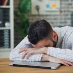 만성피로, ‘작은 변화’로 이겨내자…실생활 실천 루틴 제안 a man sitting at a desk with his head in his hands